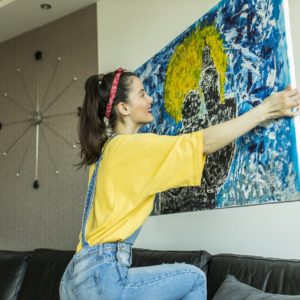 młoda kobieta wiesza na ścianie obraz